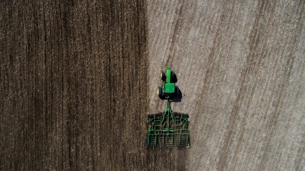 An aerial view of a tractor in a field tilling the soil. 