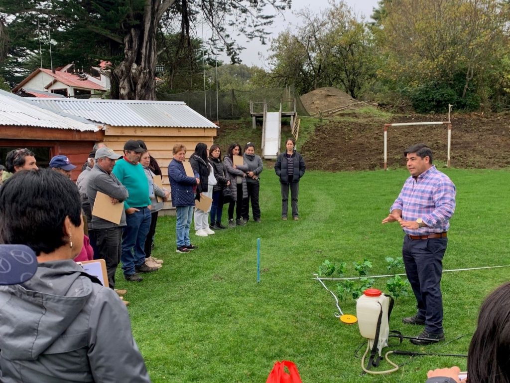 A man with a sprayer in front of him talking to a dozen of people